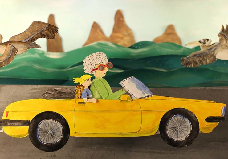 A yellow car drives on a road with waves, sea birds, and tall rocks against a light blue sky behind it. The car is two-door with the top down and animal print seat cover. A woman with white curly hair, a a green shirt, and red sunglasses with drives the car. In the passenger seat is a child with a blue shirt and yellow hair. The image is made out of cut paper.