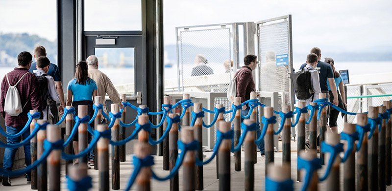 This is a photograph of people walking through the new Colman Dock passenger ferry. They are walking through the stanchions designed by artist Leo Berk. 