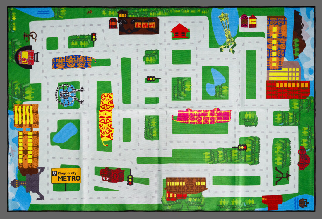 A colorful rug printed with a city street map featuring buildings, parks, ponds, and a King County Metro bus stop sign.