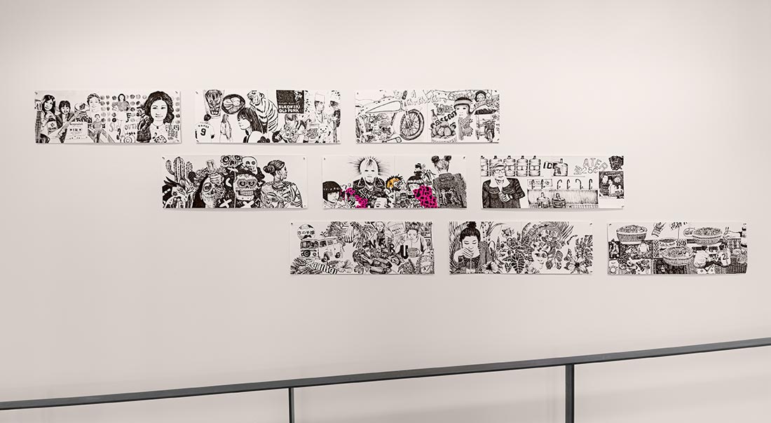 A series of black and white illustrated panels arranged in a staggered horizontal line on a white wall, depicting various people, objects, and scenes, with some areas highlighted in pink. A handrail is visible below the artwork.