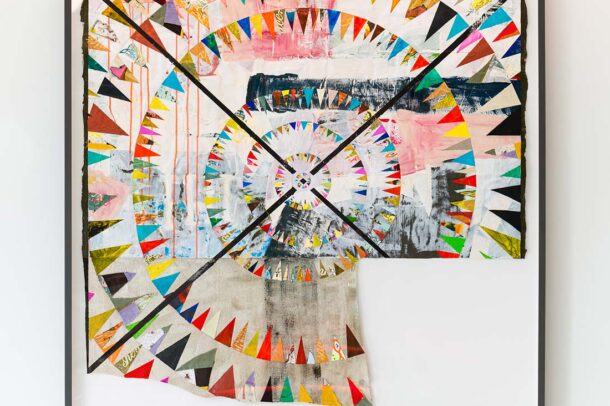 Framed abstract artwork featuring colorful, triangular shapes arranged in concentric circles with a patchwork of textures, paint splashes, and layered materials on an off-white background.