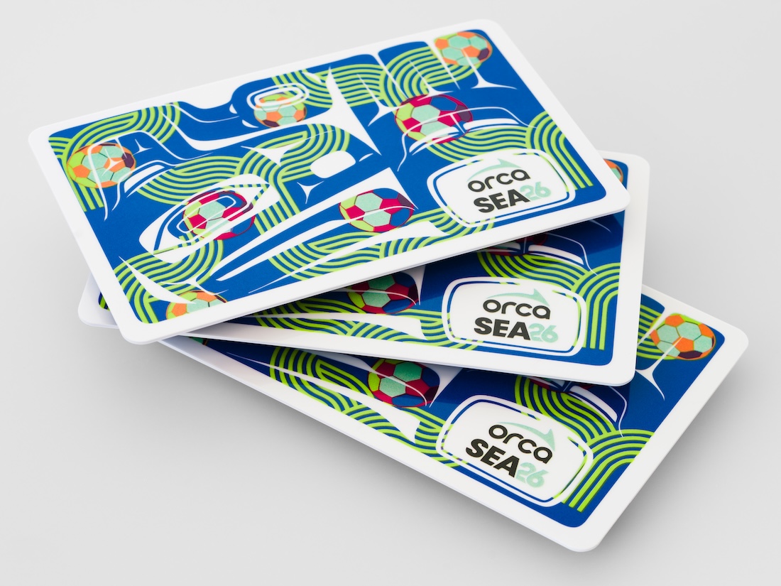 Three overlapping ORCA SEA 2026 transit cards with a colorful abstract design featuring green lines and multicolored shapes on a blue background, placed on a light surface.